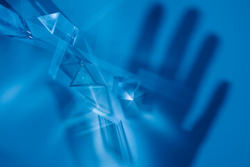 Wall Mural - Transparent prisms and cubes with rays of the color spectrum. Abstract background with reflection and hand shadow. The concept of scientific experiments, medicine and innovation