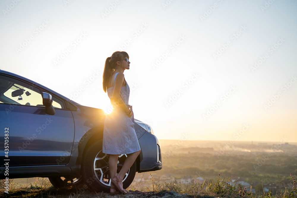 Happy young woman driver in blue dress leaning on her car enjoying warm summer day. Travelling and vacation concept. - obrazy, fototapety, plakaty 