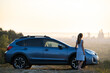 © bilanol - Young female driver resting near her car enjoying warm summer evening. Travel and getaway concept.