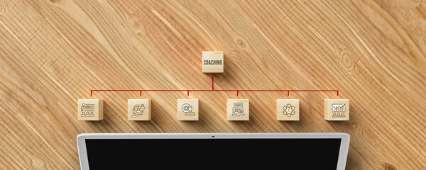 Wall Mural - cubes with message COACHING and business symbols above a laptop on wooden background