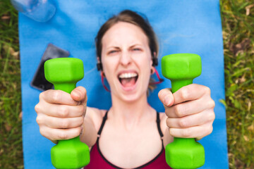 Pretty young woman holding dumbbells, doing hard workout outside. Fit girl screaming to succeed gym. Concept about lifestyle, sport, leisure and people.