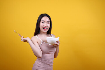 Wall Mural - Beautiful young south east Asian woman holding chines empty chopstick Chinese soup spoon bowl utensil pretend acting posing see eat taste smell feed offer satisfaction yummy yellow orange background