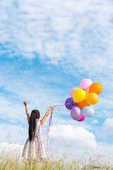 Wall Mural - Cheerful cute girl holding balloons running on green meadow white cloud and blue sky with happiness. Hands holding vibrant air balloons play on birthday party happy times summer on sunlight outdoor