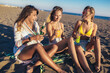 © Mediteraneo - Happy young women sitting on the beach drink beer and juice. Group of friends enjoying on beach holiday.