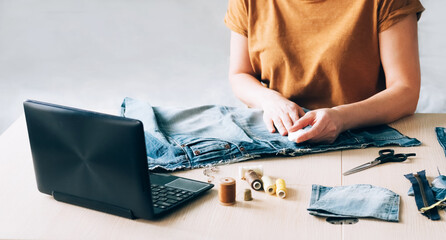 Wall Mural - A woman is engaged in online training and looks at sewing lessons on a laptop. DIY Hobby Reuse Recycling Zero Waste