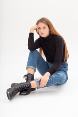 portrait of young attractive caucasian woman with long hair in black turtleneck, blue jeans isolated on white studio background. skinny pretty female sits on cyclorama. model tests of beautiful lady