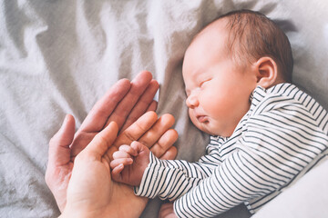 Family happiness concept. Sleeping newborn in first days of life at home. Father and mother holding baby hand.