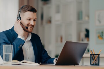 smiling young manager sitting at desk at home and taking part in online meeting