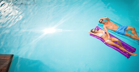 Wall Mural - Composition of couple lying on inflatables in swimming pool with glowing light and copy space