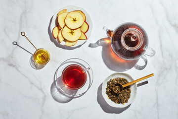 Wall Mural - Fruit tea with apples and thyme and honey in glass teapot and cup on white background with hard shadows