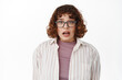 © Cookie Studio - Girl freaks out, look at camera with panic, stare alarmed and cringe, scared of something bad coming, standing in glasses and casual clothes against white background
