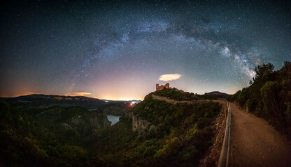 Wall Mural - Panoramic of the Milky Way over a medieval castle on a lake. Beautiful views of the Milky Way above a castle on a mountain hill surrounded by a large lake