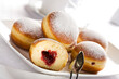 Bismarck doughnuts filled with jam and decorated with confectioner's sugar on a platter with pastry tongs