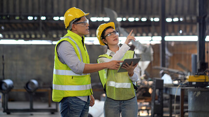 asian industrial Engineer manager man wearing eyeglass and helmet   discussion with mechanic worker woman while using digital tablet checking industry manufacturing large factory . inspection