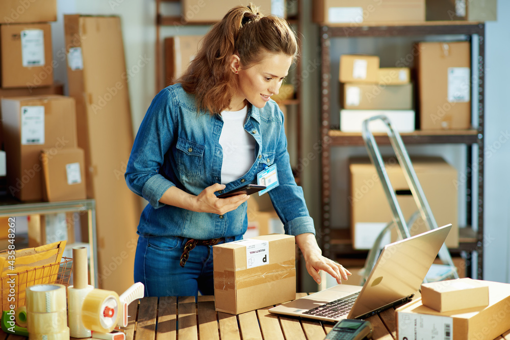 happy female in jeans using phone applications in warehouse - obrazy, fototapety, plakaty 