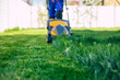 Young man mows the lawn using an electric lawn mower in a special worker suit near a large country house in the backyard