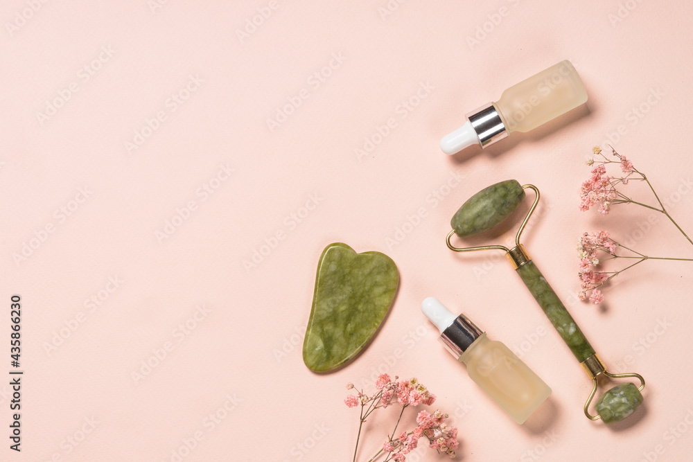 Jade roller and gua sha stone massager at pastel background. Anti-aging therapy. Top view. - obrazy, fototapety, plakaty 