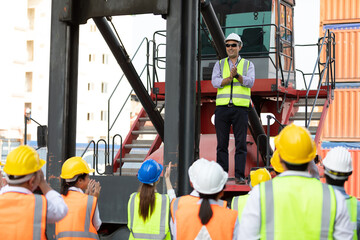 warehouse boss engineer standing on crane car with factory workers clapping hands for congratulations work in containers warehouse storage