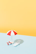 White And Red Beach Umbrella, Sun Chair, Blue And White Striped Towel And Life Buoys On Blue And Yellow Background. Beach Set For Sunny Days. Summer Holiday Concept. Copy Space. Vertical Image.