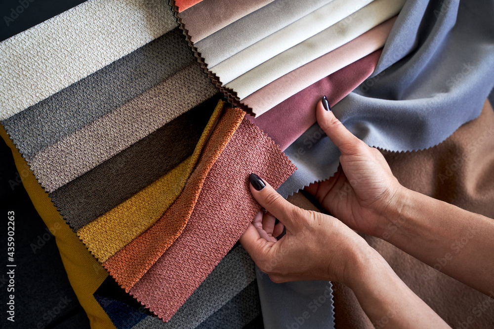 Choosing upholstery fabric color and texture from various colorful samples in a store. Female customer hands touching textile. - obrazy, fototapety, plakaty 