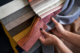 Fototapeta  - Choosing upholstery fabric color and texture from various colorful samples in a store. Female customer hands touching textile.