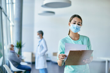 Young nurse with protective face masks going through medical reports while working at clinic.