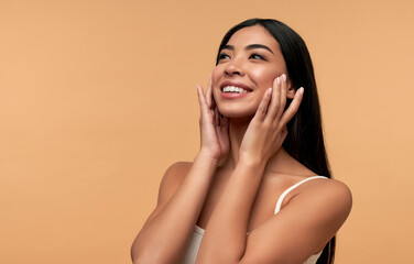 Wall Mural - Young Asian woman with clean healthy glowing skin in white top isolated on beige background. Facial skin care concept, spa, cosmetology, plastic surgery.