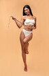 © Valerii Apetroaiei - Young Asian woman in white lingerie with a toned body and a slender figure with a measuring tape on a beige background. Sports, healthy lifestyle. Spa body care. Plastic surgery.