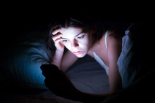 A Young Girl Lies In Bed And Cannot Sleep, Reads And Chat On Social Networks On A Smartphone. A Woman With Insomnia Is Watching A Video Online On A Device.