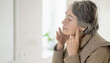 © Zhanna - An elderly woman puts her fingers on the lymph nodes in her neck and looks at herself in the mirror. The pensioner takes care, monitors thyroid hormones and the health of the endocrine system.