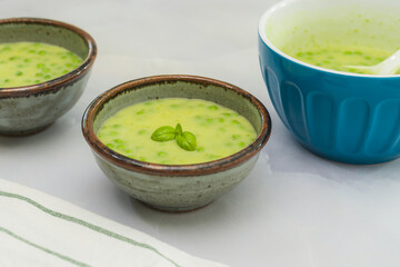 Wall Mural - Creamy celery soup with green peas and fresh basil close up in bowls on light grey marble background