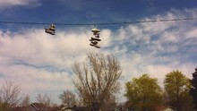 Slow Drone Pan Across Telephone Wire With Tennis Shoes Trainers On It With Blue Sky And White Clouds, Spring Trees And Rural Suburban Neighborhood Houses In Background. In 4k Real Time.