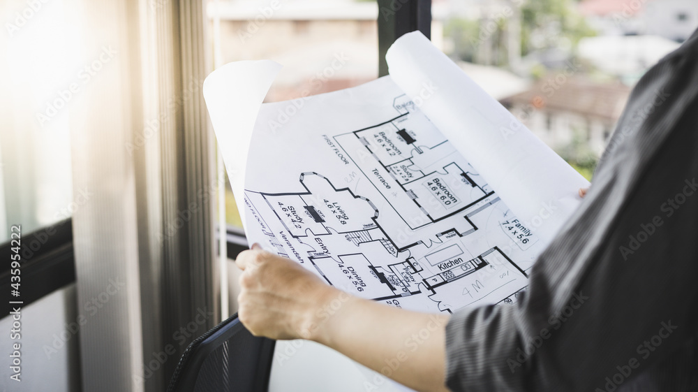 Architectural building design and construction plans with blueprints, Young man was designing a building or architecture with a ruler, pen, pencil, tape measure, architect hat and other equipment.