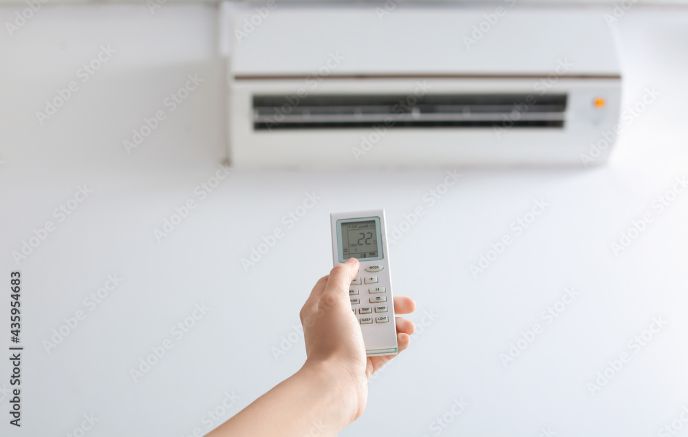 Female hand with air conditioner remote control indoors, closeup
