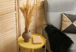 Vase with wheat spikelets on table and armchair near folding screen