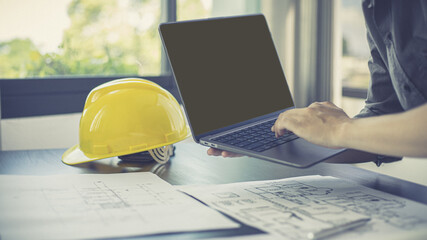 Young man with a laptop plotting a system of building structures in blueprints, Architects or engineers are designing buildings using computers to calculate the physical structure to be correct.