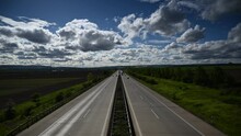 A 4K Time-lapse Of Driving Cars On A Dual Carriageway Road Through Farmlands Under White Fluffy Clouds