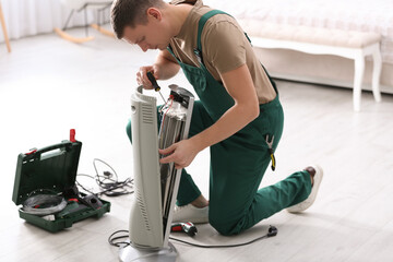 Canvas Print - Professional technician repairing electric ultrared heater with screwdriver indoors