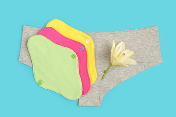 Wall Mural - Colored eco reusable menstrual pads and grey panties on blue background. Health care and zero-waste, no plastic concept. Top view Flat lay Close-up