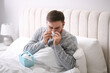 © New Africa - Young man suffering from runny nose in bed indoors