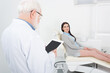 © LIGHTFIELD STUDIOS - senior dentist looking at blank screen tablet in front of blurred patient in dental chair in clinic.