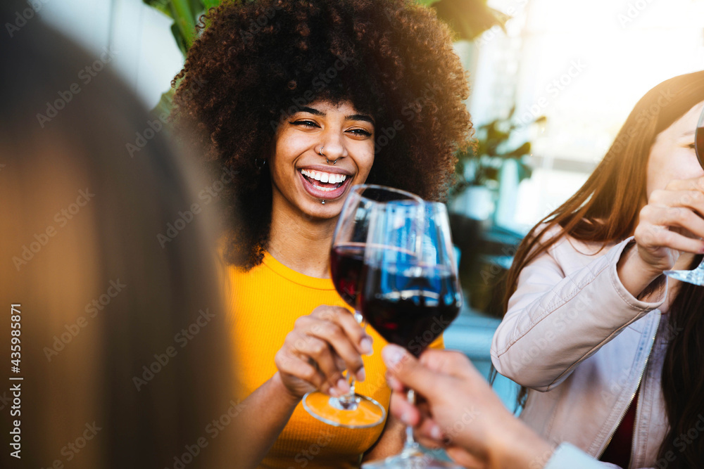 Happy african american woman drinking red wine at bar restaurant - Multiracial friends having fun celebrating at dinner time toasting drinks - Friendship concept - obrazy, fototapety, plakaty 