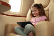 © New Africa - Cute little girl using tablet in airplane during flight