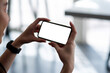 © amnaj - Close up shot of a woman holding a smartphone horizontally blank white screen. Mock up.