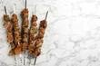© New Africa - Metal skewers with delicious meat on white marble table, flat lay. Space for text