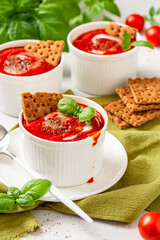 Wall Mural - Tomato soup with crispbread and basil in white bowls on a gray background. Tasty summer food.