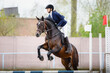 portrait of mare horse and beautiful woman rider jumping during equestrian show jumping competition in daytime in spring