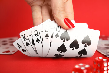 Woman holding playing cards with royal flush combination at red table, closeup