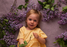 A Beautiful Girl In A Yellow Dress Is Lying, And Lilac Branches Are Lying Around Her