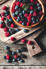 Wall Mural - Ripe blackberries with leaves in a bowl on a wooden board on a dark background